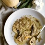 cooked butternut squash ravioli in sage brown butter sauce on a plate with fork