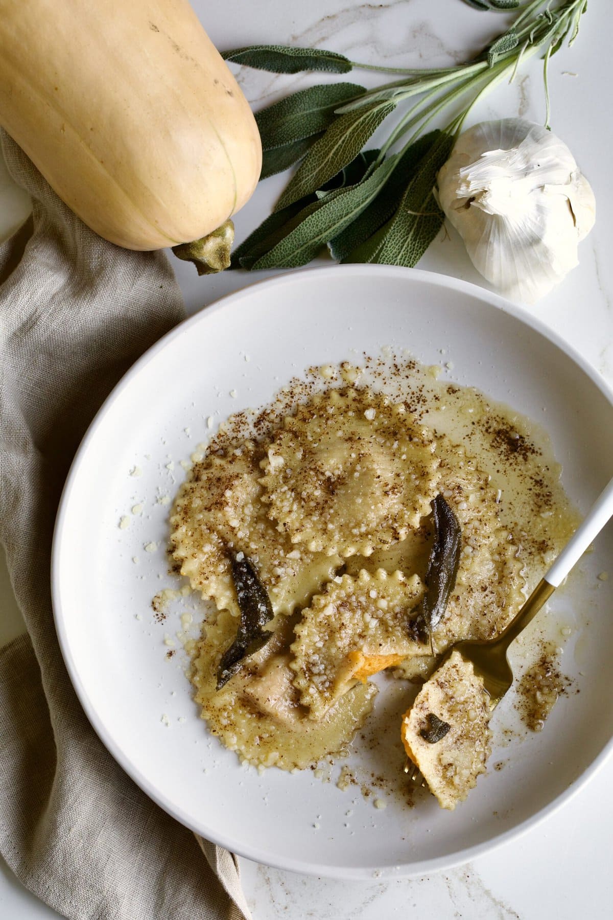 cooked butternut squash ravioli in sage brown butter sauce on a plate with fork