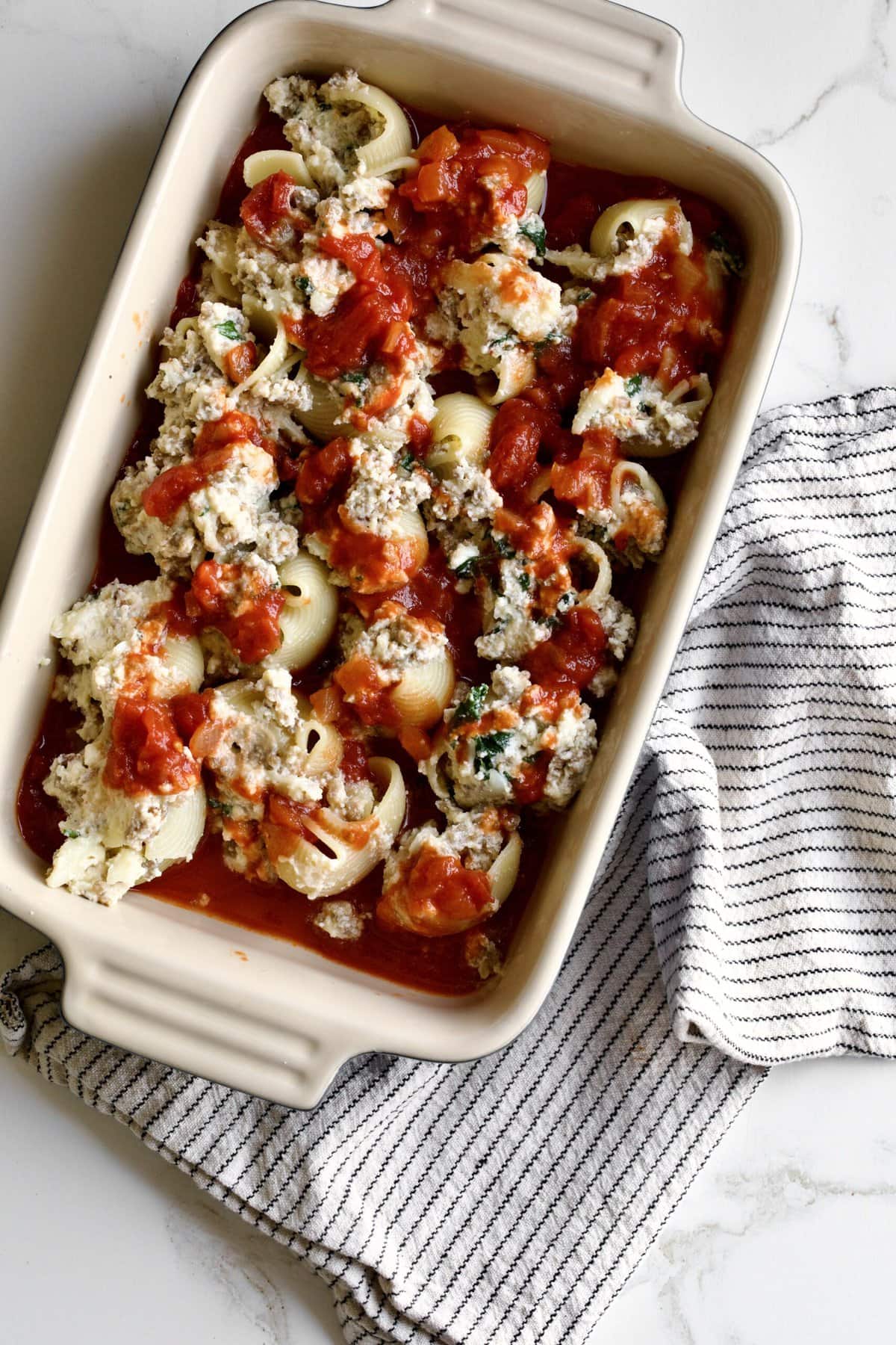 stuffed shells covered in red sauce ready to bake. Smaller baking dish to freeze.