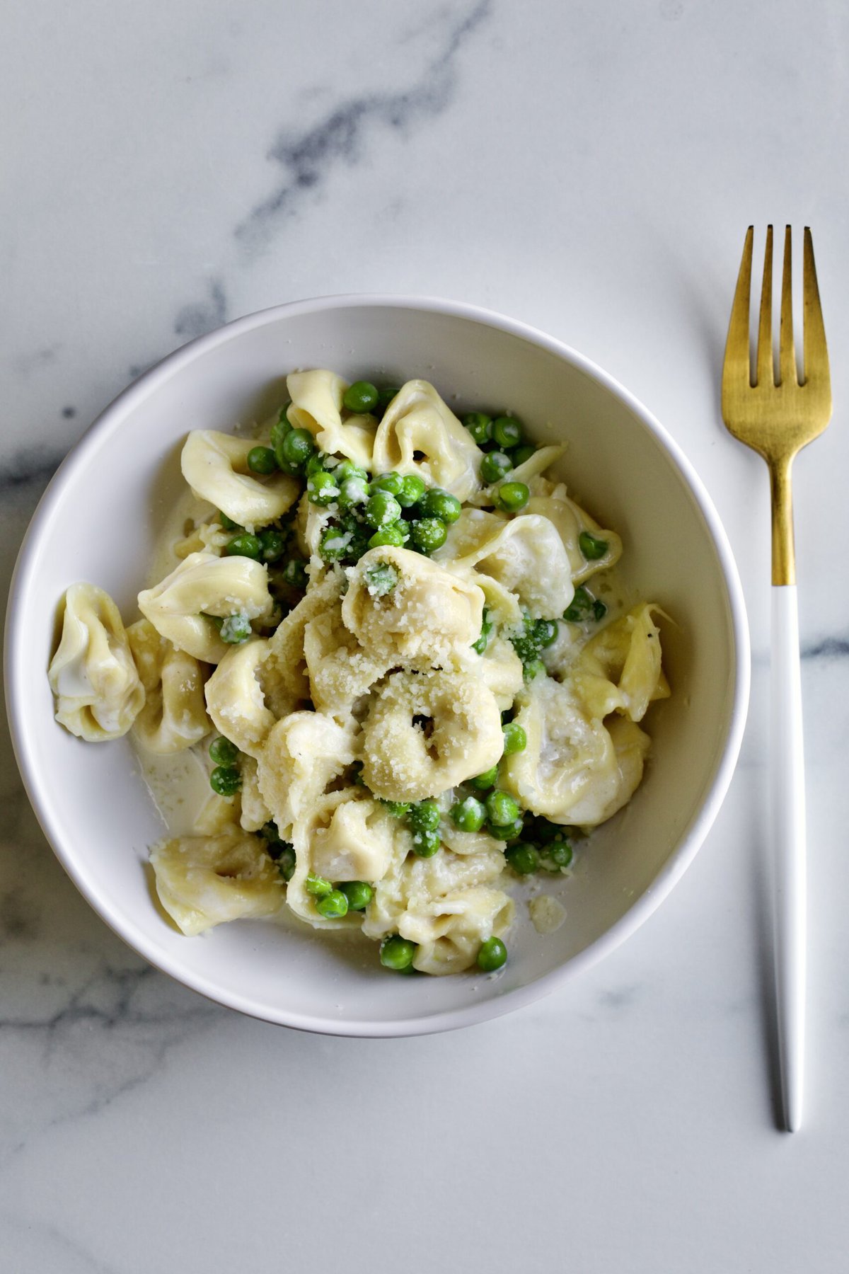 bowl of Tortellini Alla Panna Recipe with Peas with a fork next to it.