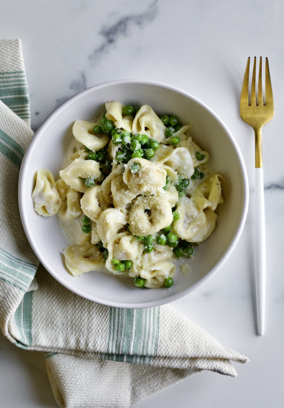 bowl of Tortellini Alla Panna Recipe with Peas with a fork and napkin next to it.