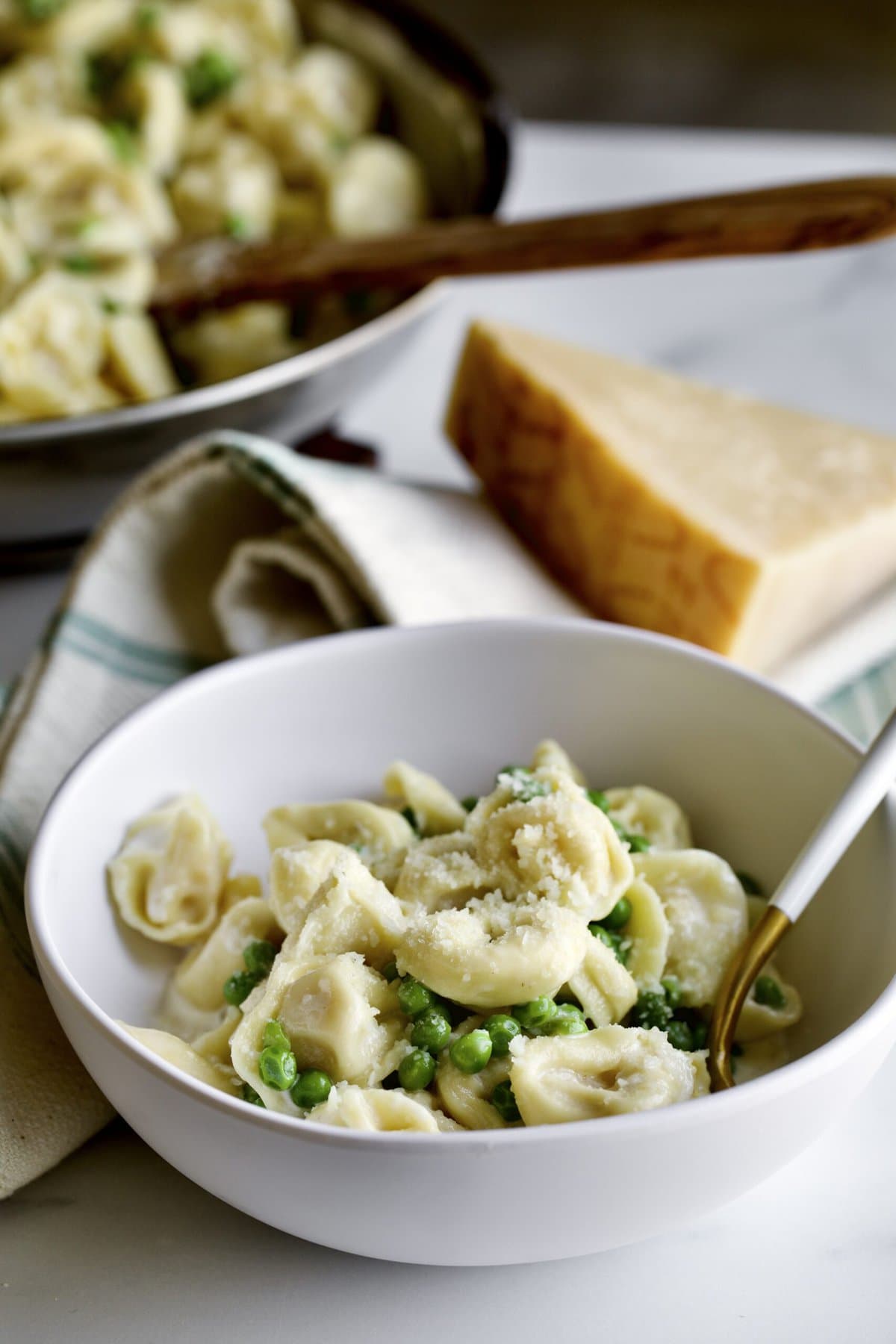 bowl of pasta with fork in it and wedge of parmigiano cheese in the background. 