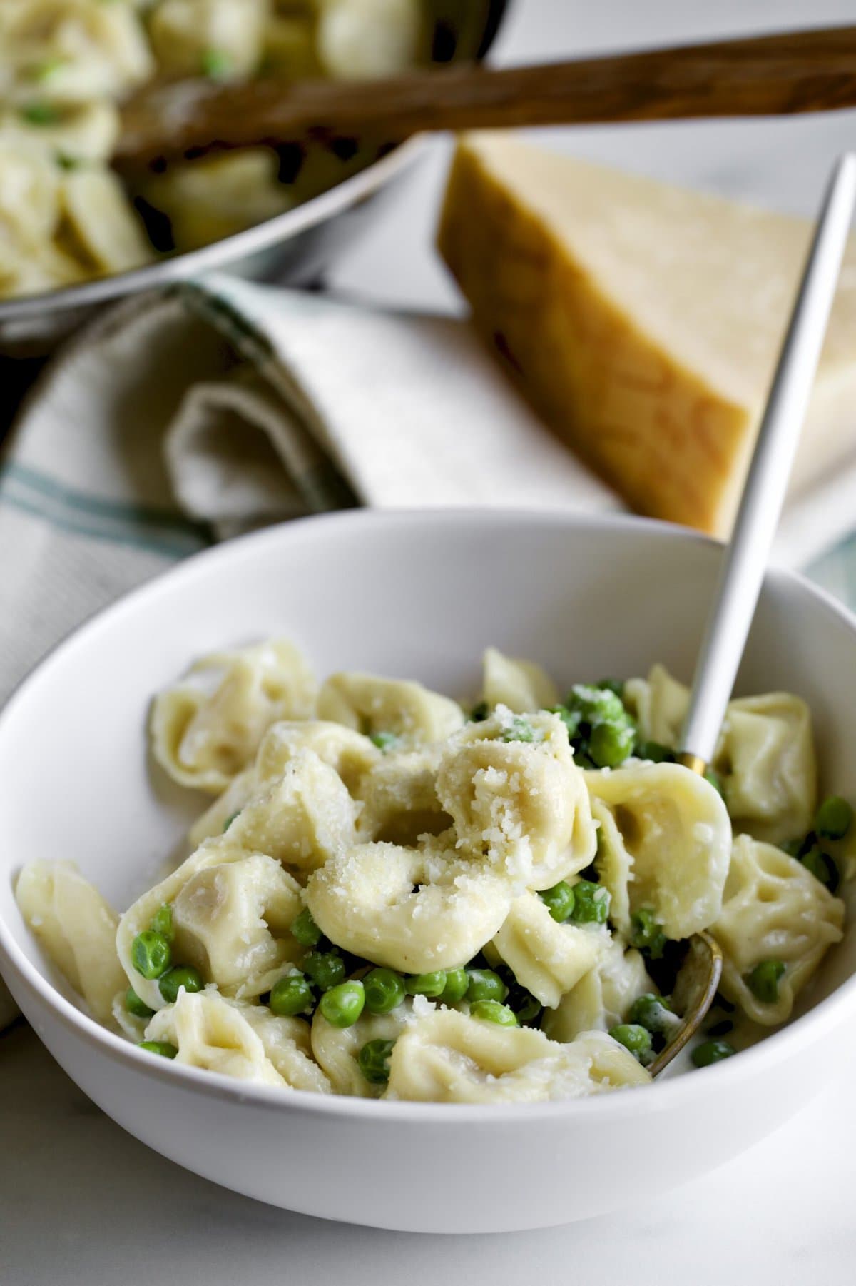 close up ofbowl of Tortellini Alla Panna Recipe with Peas with a fork and napkin next to it.