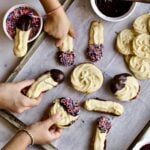 People grabbing chocolate-dipped Italian butter cookies from a lined baking sheet.