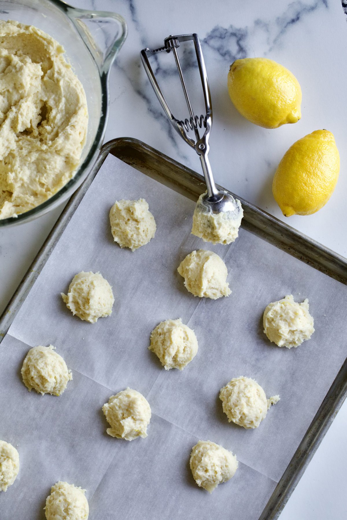 uncooked lemon ricotta cookies on a cookie sheet with cookie scoop on the side.