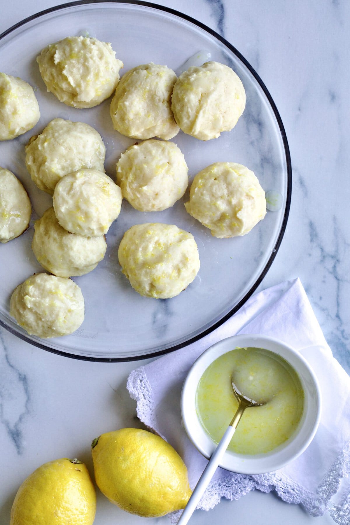 Italian lemon ricotta cookies on glass plate with lemon glaze on the side.