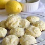 lemon ricotta cookies on a glass plate with lemons in the background.