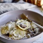 plated mushroom ravioli with cream sauce with rosemary as garnish.