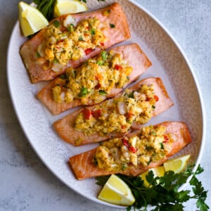 Crab and shrimp stuffed salmon on a service platter with lemons and greens.