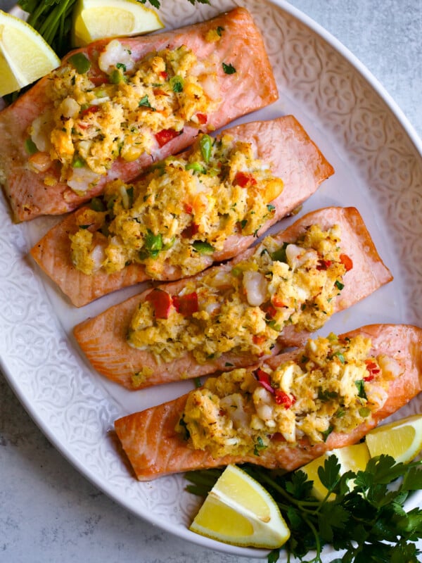 Crab and shrimp stuffed salmon on a service platter with lemons and greens.