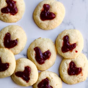 Heart thumbprint cookies with jam on a marbled surface.