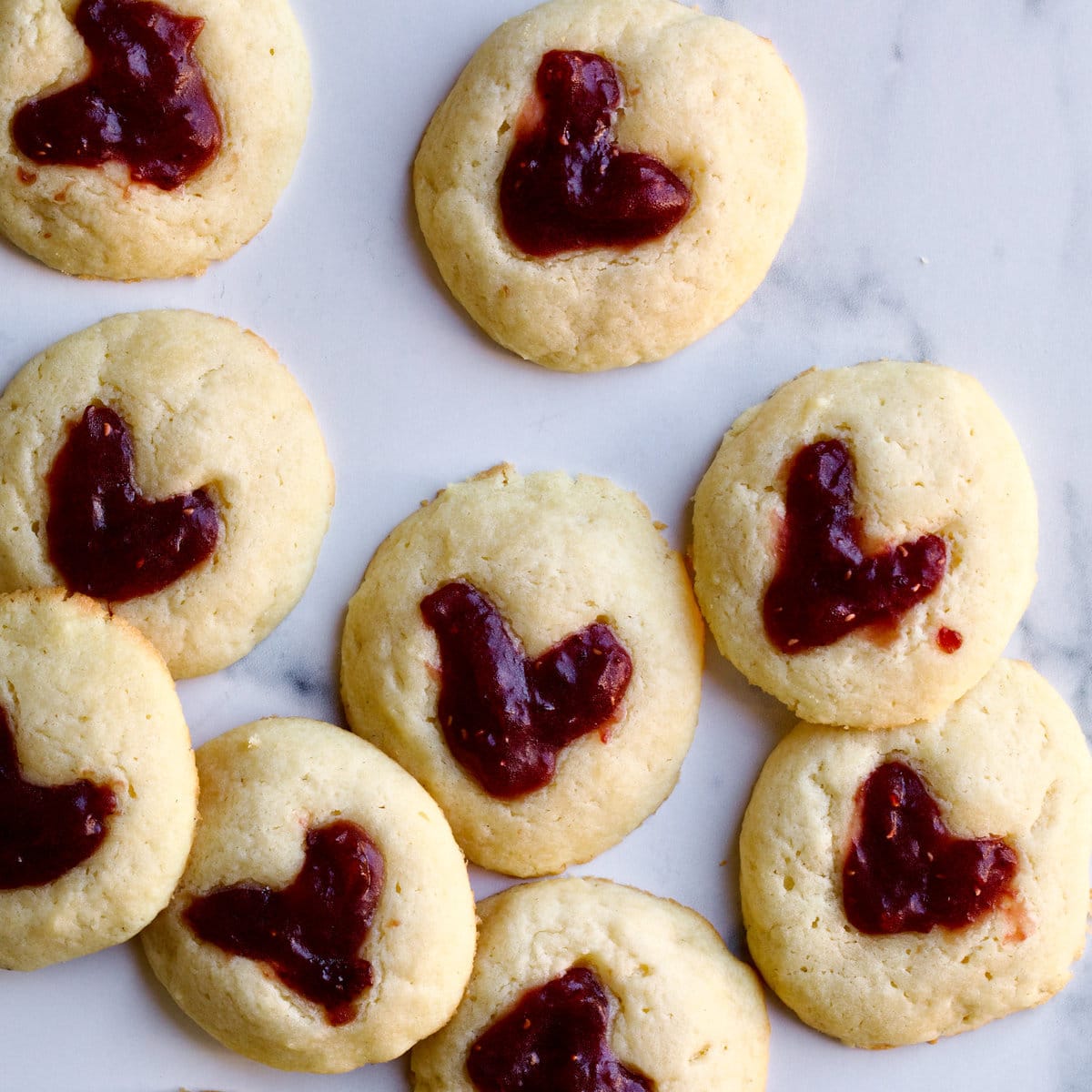 Heart thumbprint cookies with jam on a marbled surface.