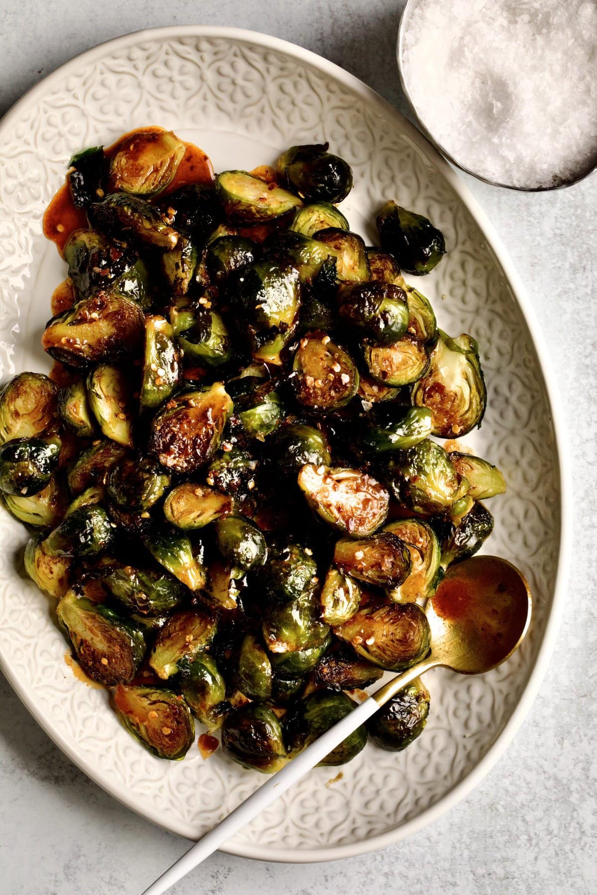 Crispy Brussels Sprouts Recipe on a cream colored serving platter. with serving spoon