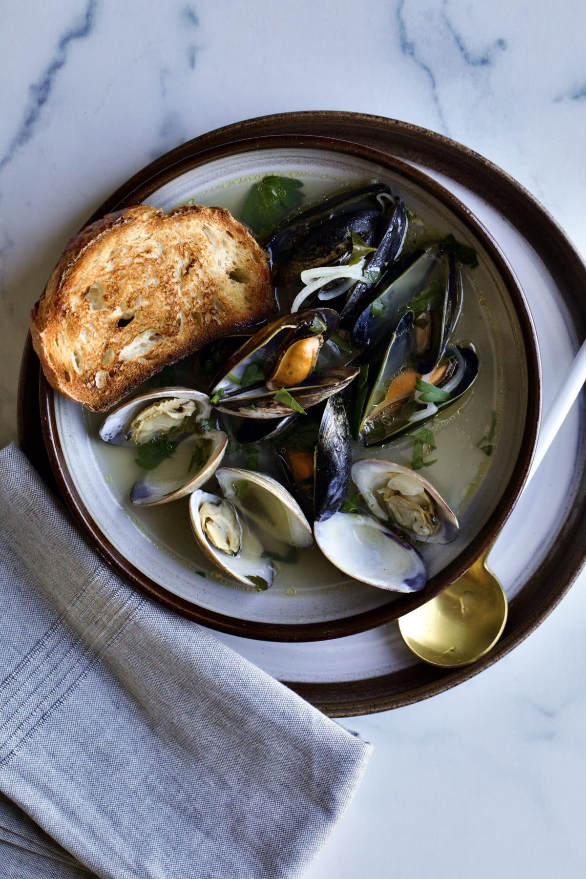 Steamed Mussels and Clams Recipe (with Wine and Garlic) in a bowl with spoon and toasted bread.