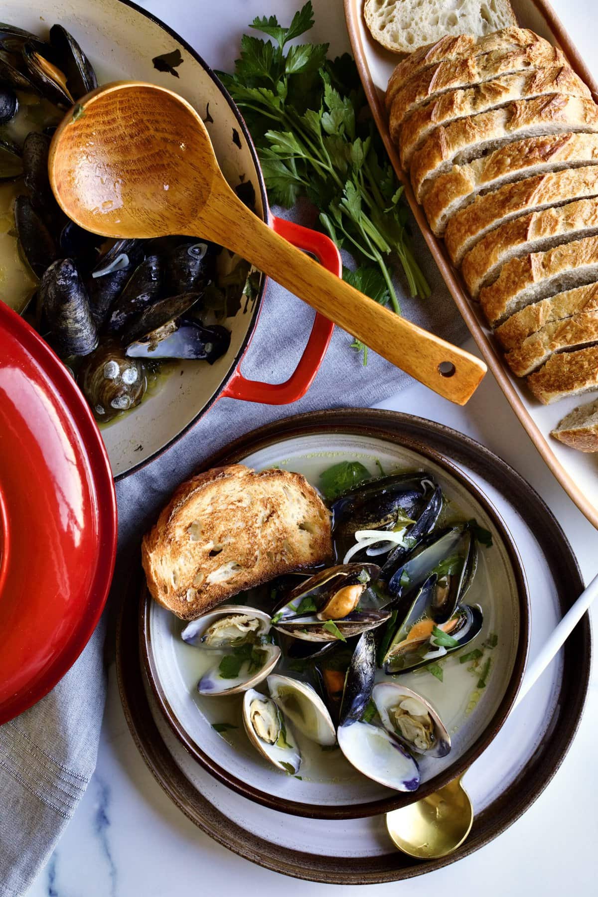 pot with mussels and clams, bowl with  mussels and clams and toasted bread. 