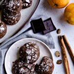 chocolate spice cookies on a plate with pieces of chocolate, orange and spices, in the background.