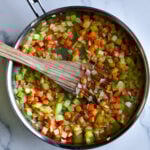 Wooden spatula in a pan with onion, carrot, and celery.