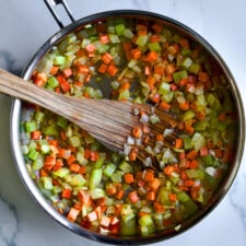 Wooden spatula in a pan with onion, carrot, and celery.