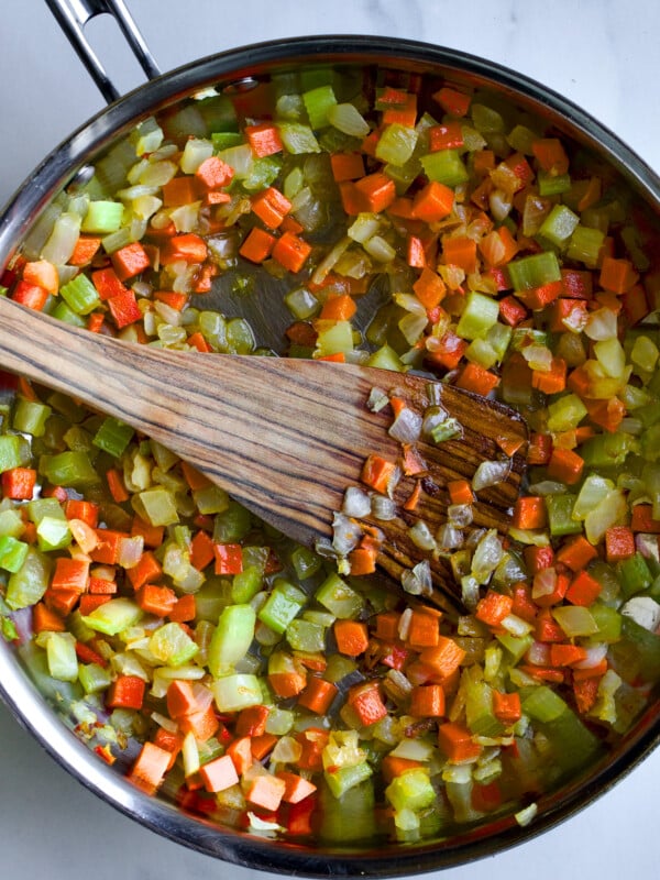 Wooden spatula in a pan with onion, carrot, and celery.