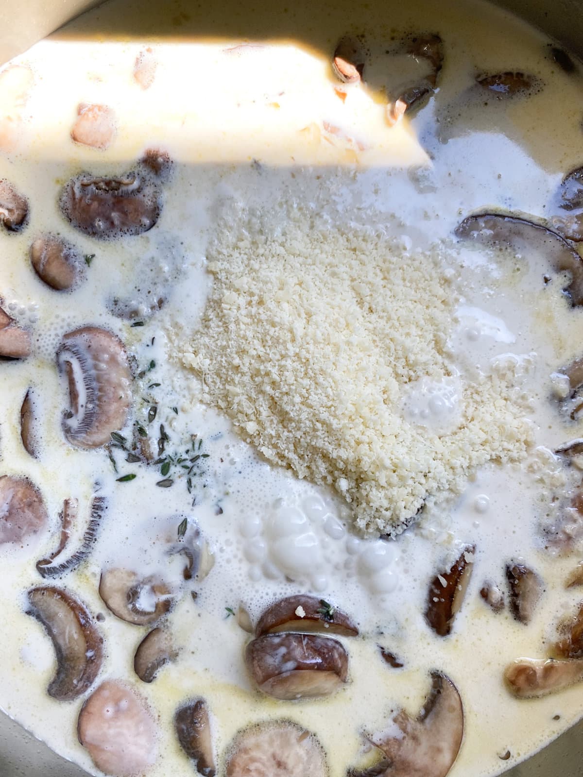 How to make mushroom ravioli in cream sauce- adding parmigiano cheese and herbs to mushroom cream sauce.