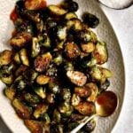 Crispy Brussels Sprouts Recipe on a cream colored serving platter. with serving spoon