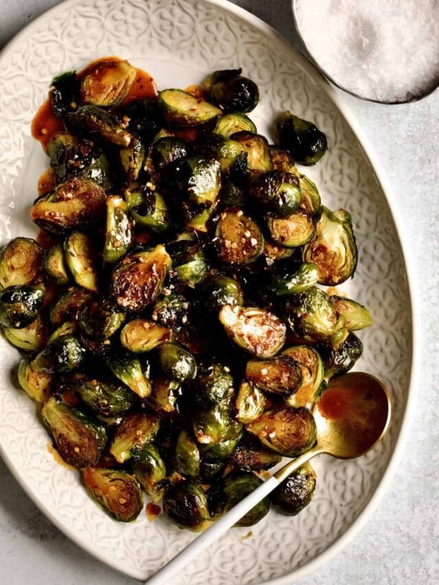 Crispy Brussels Sprouts Recipe on a cream colored serving platter. with serving spoon