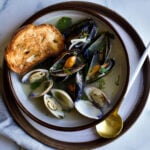 Steamed mussels and clams on a plate with bread and a spoon.