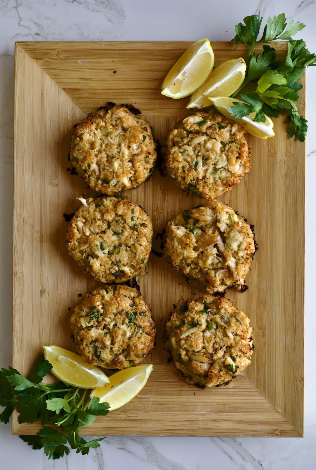 crab cakes displayed on wooden board with lemon and parsley.