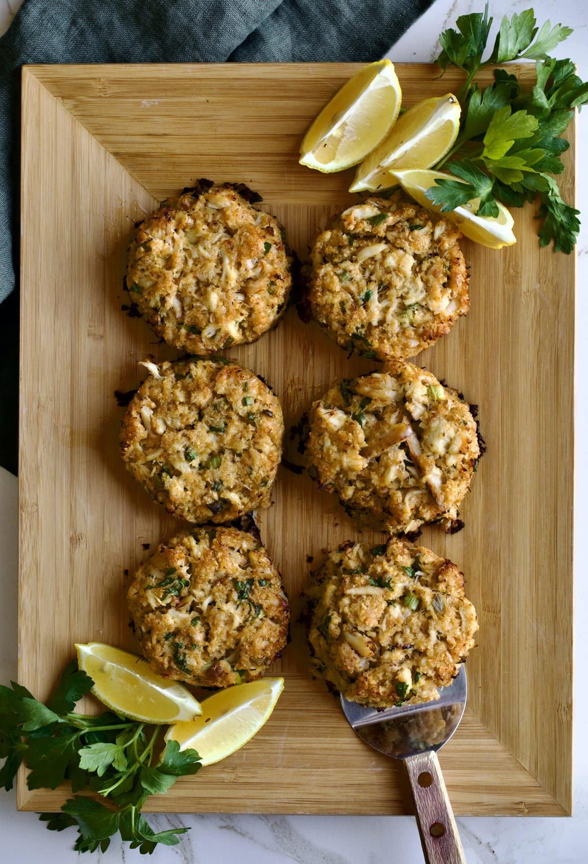 crab cakes displayed on wooden board with lemon and parsley.