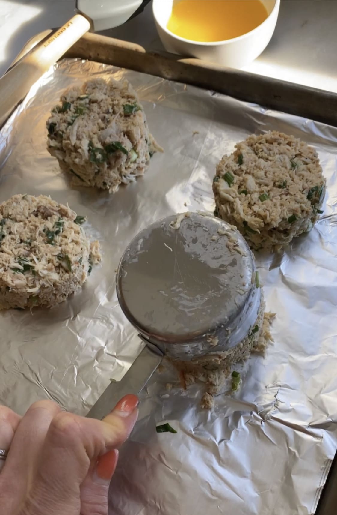 Measuring spoon portioning crab cakes onto foil.