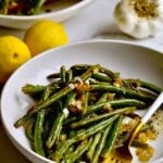 Roasted Green Beans Recipe with Garlic and Lemon on a plate with a serving plater in the background.