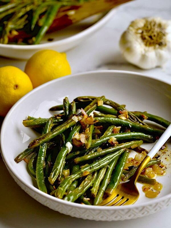 Roasted Green Beans Recipe with Garlic and Lemon on a plate with a serving plater in the background.