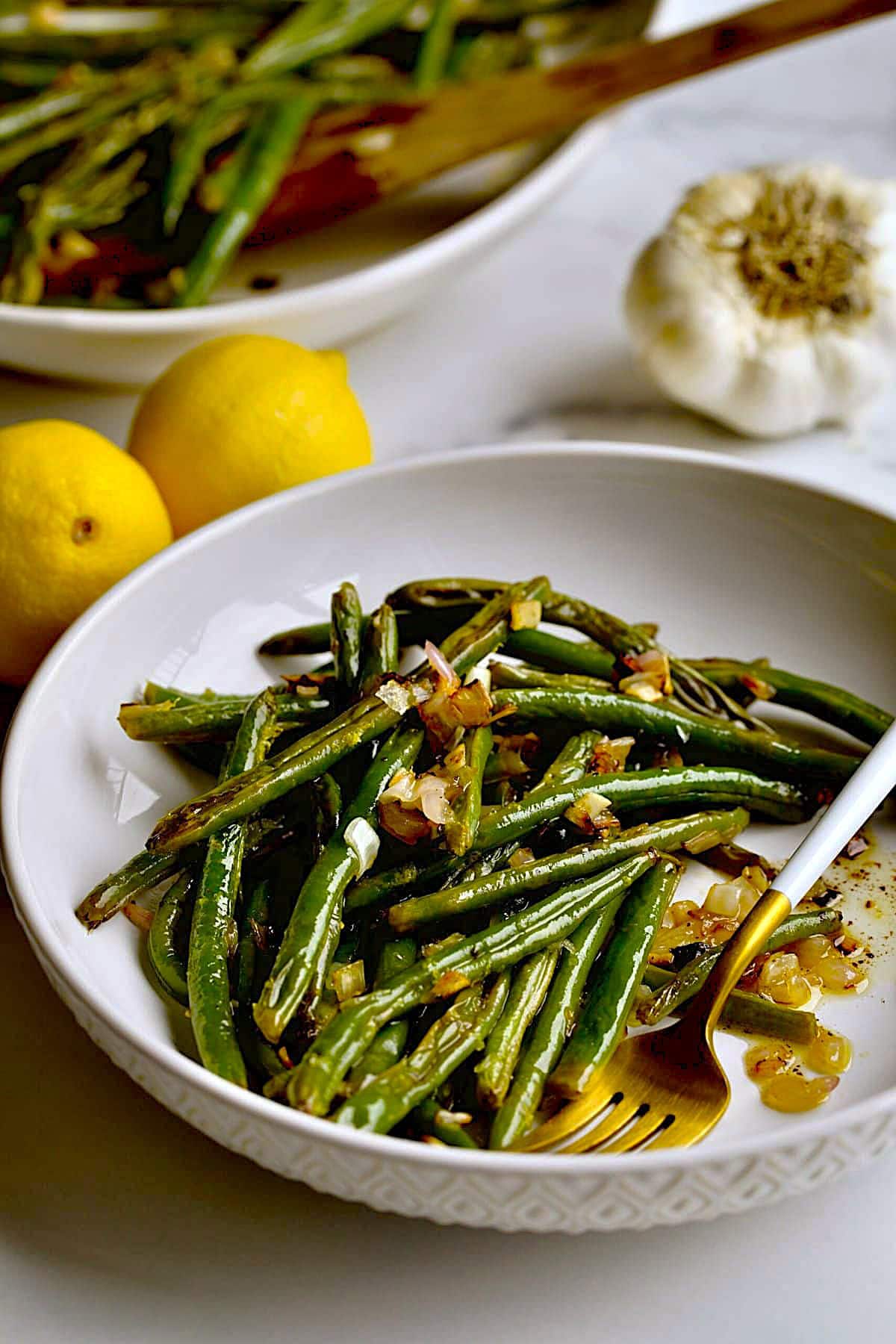 Roasted Green Beans Recipe with Garlic and Lemon on a plate with a serving plater in the background.