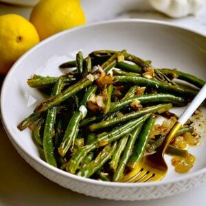 Roasted Green Beans Recipe with Garlic and Lemon on a plate with a serving plater in the background.