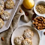 pignoli cookies on a platter with almonds and pine nuts around it.