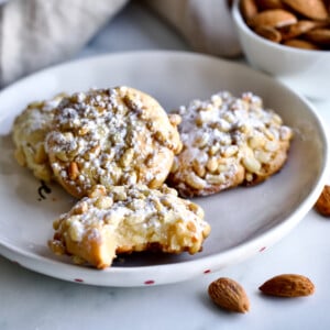Italian Pignoli Cookies, one of which is missing a bite, on a plate.