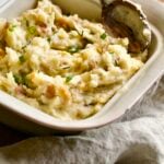 red skin mashed potatoes in a square serving platter with a wooden spoon.