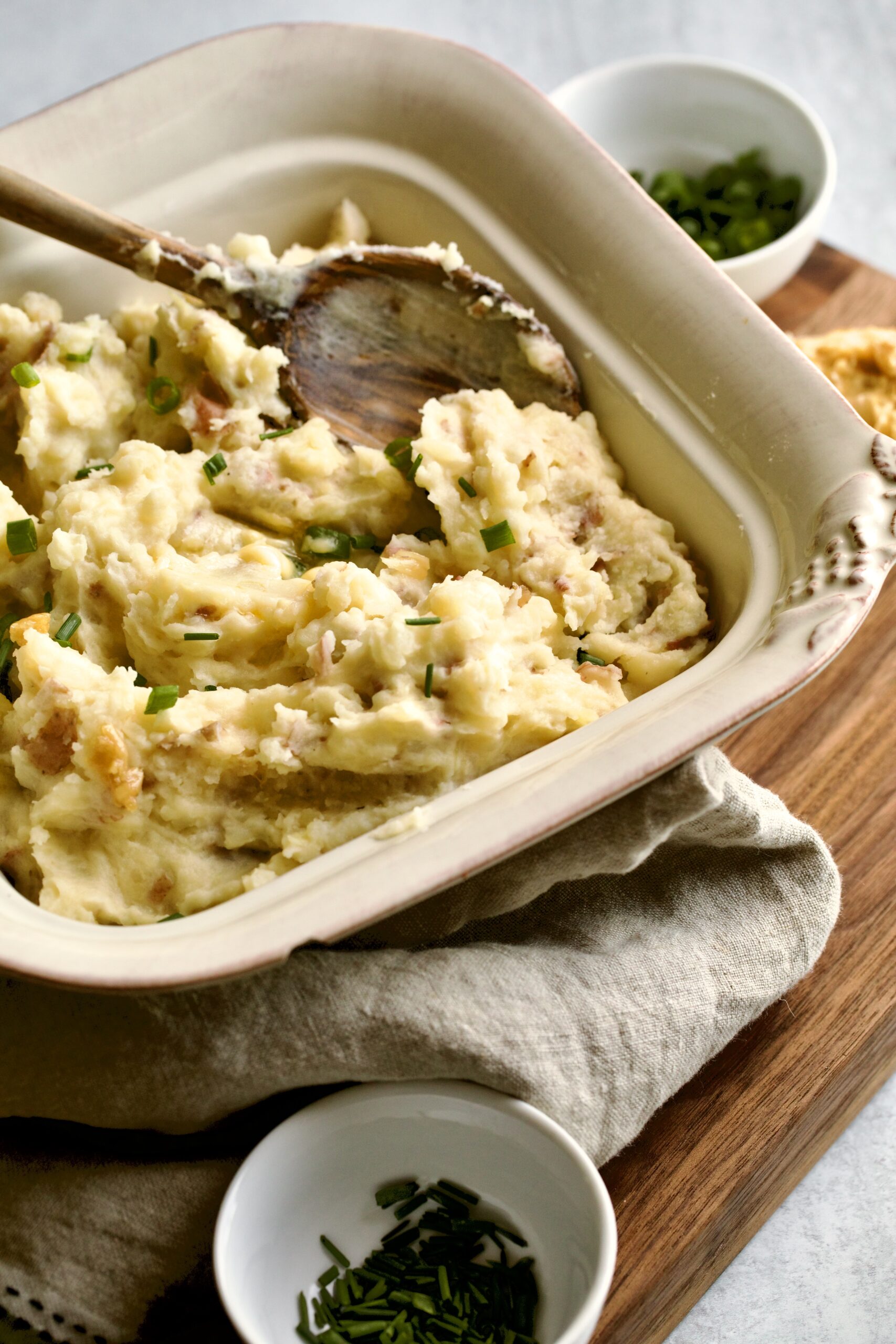 red skin mashed potatoes in a square serving platter with a wooden spoon.