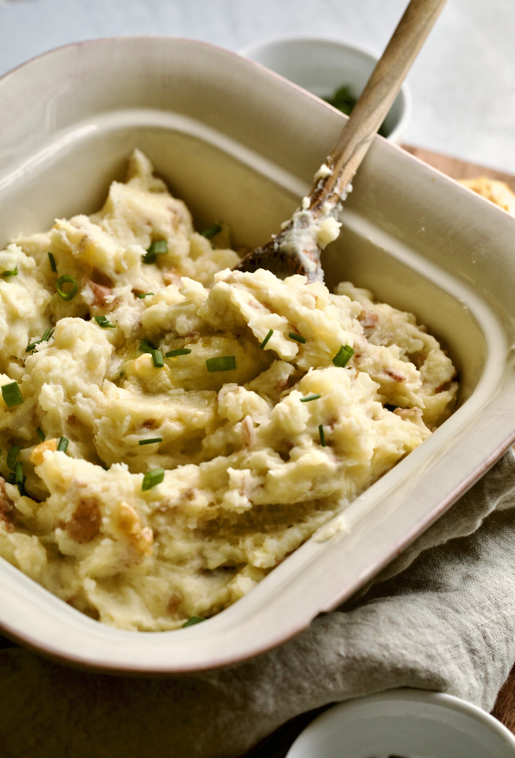 red skin mashed potatoes in a square serving platter with a wooden spoon.