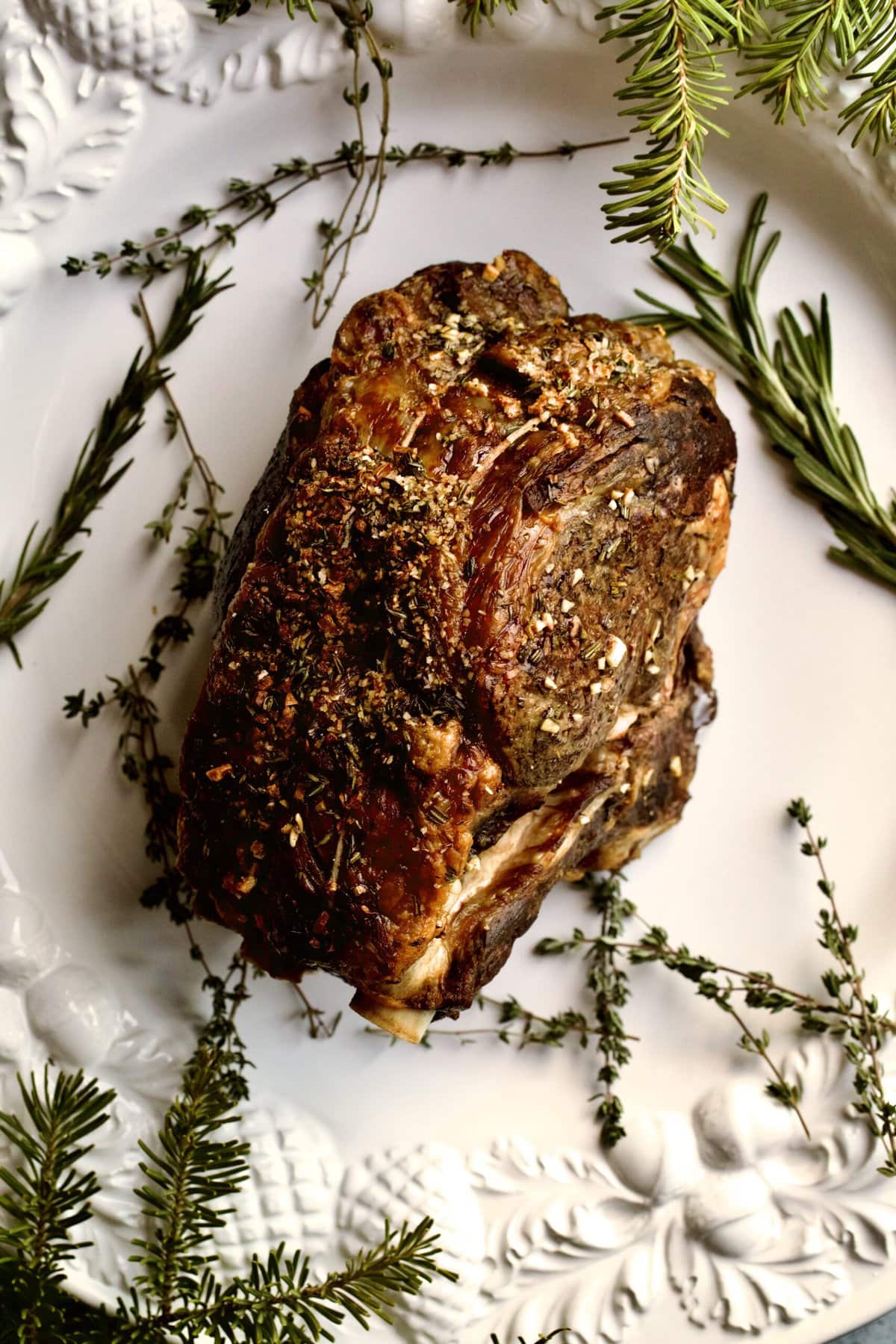 whole roast prime rib on serving plate with herbs.