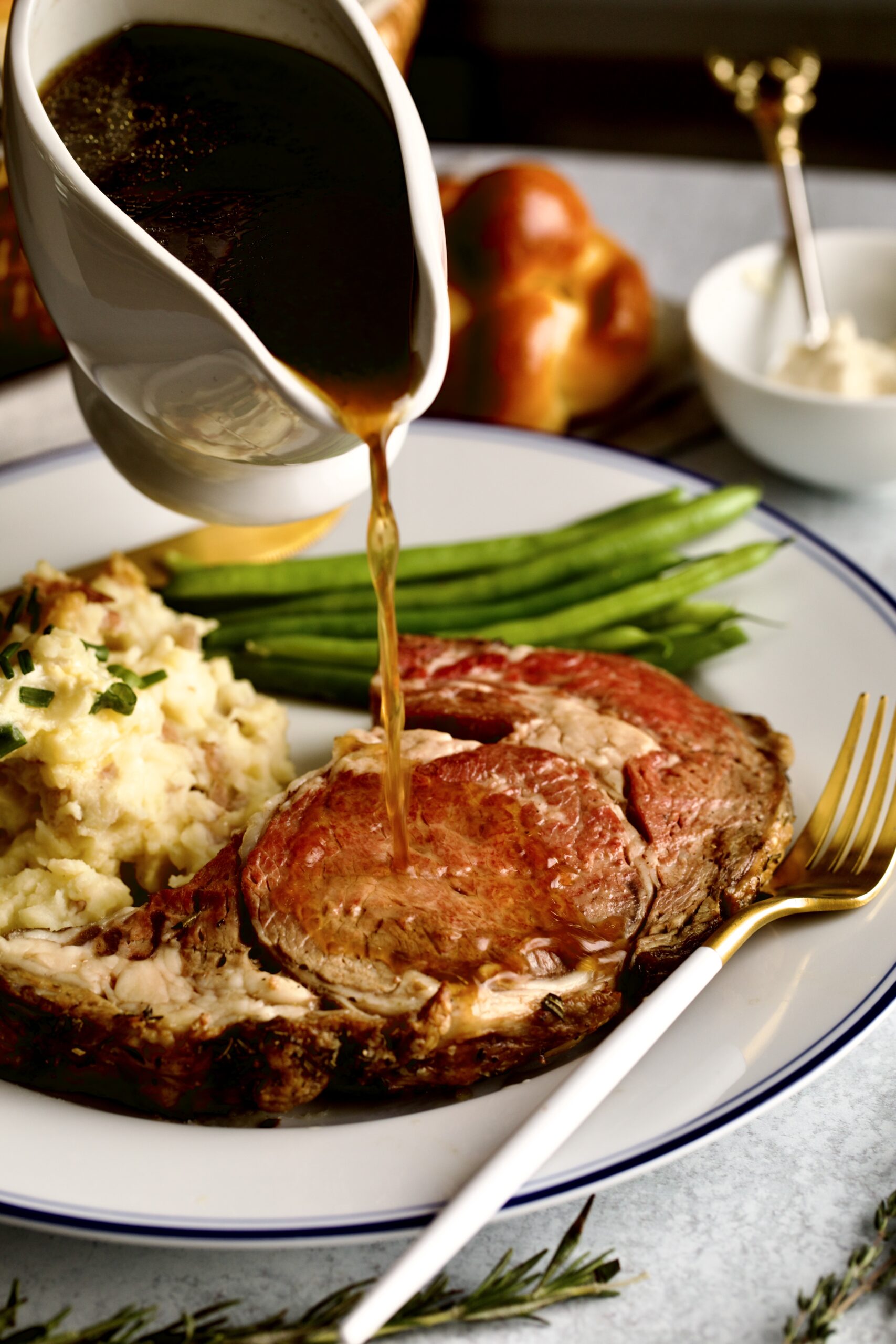 pouring au jus sauce over prime rib and mashed potatoes.