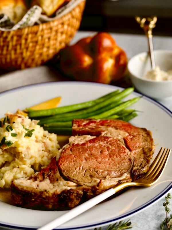 prime rib slice on a plate with garlic red shin mashed potatoes and green beans.