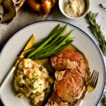 prime rib slice on a plate with garlic red shin mashed potatoes and green beans. Horseradish and dinner roll in background.