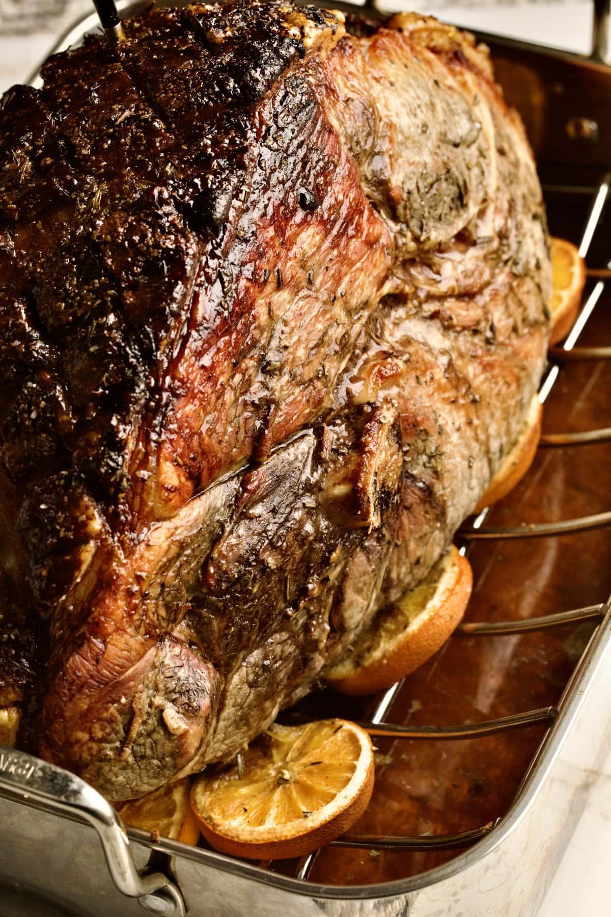 Cooked fresh ham roast with oranges coming out of oven in roasting pan.