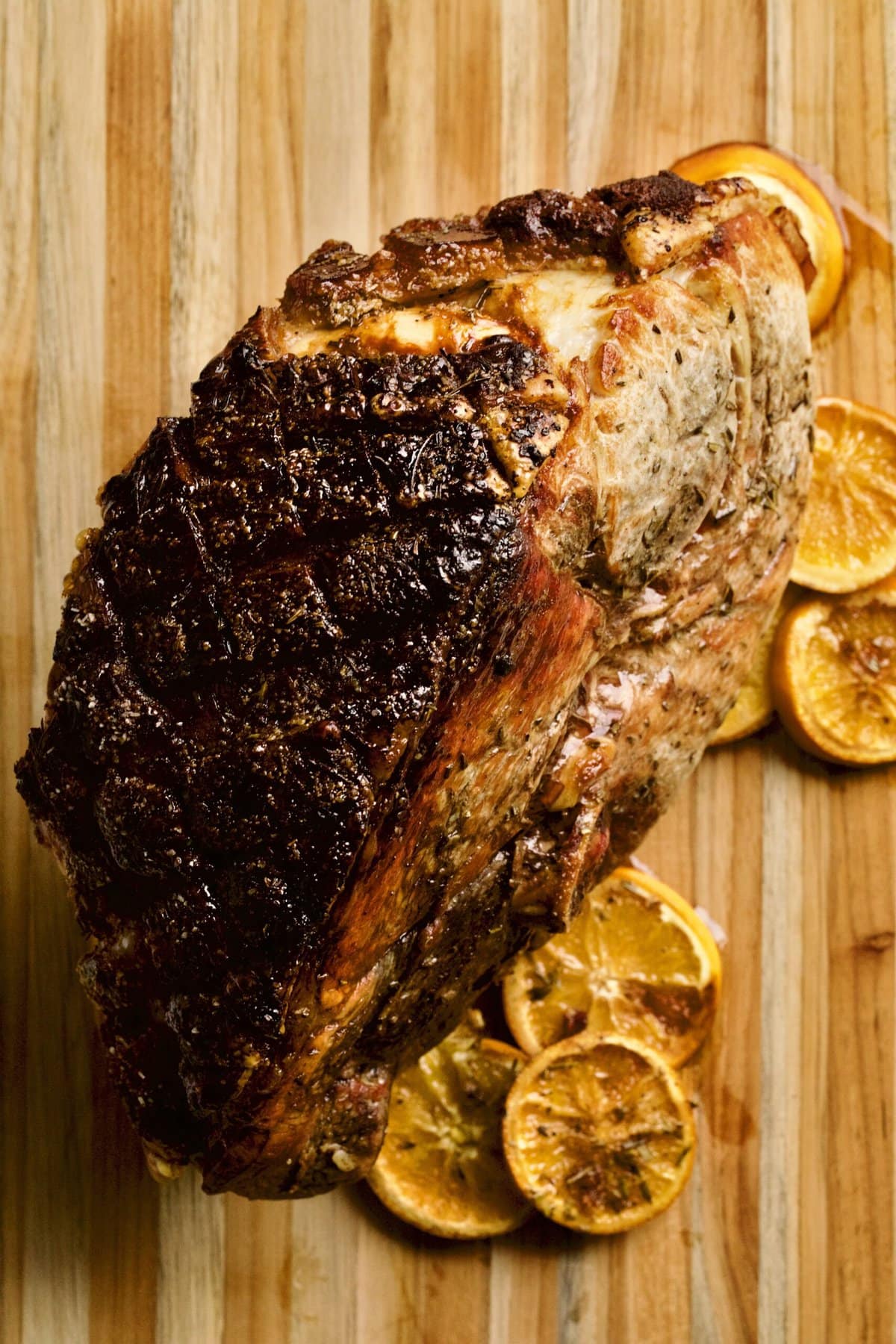 Cooked fresh ham roast with oranges coming out of oven ion wood cutting board.