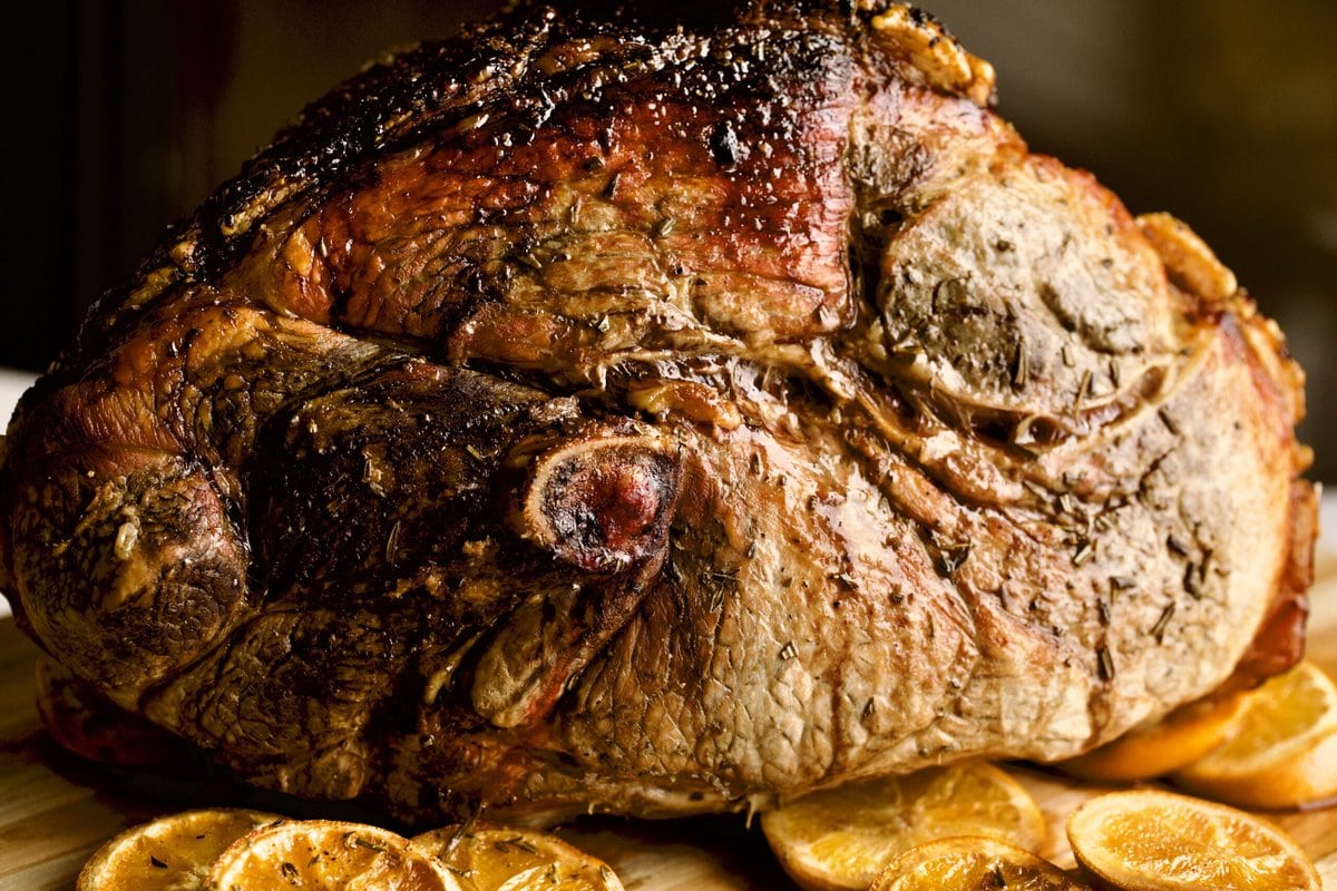 Cooked fresh ham roast with oranges coming out of oven ion wood cutting board.