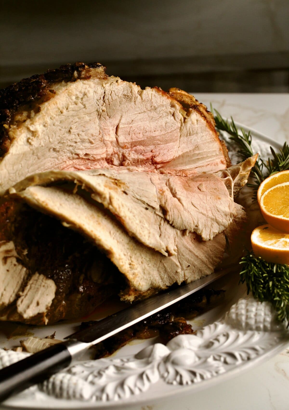 Cooked fresh ham roast with oranges coming out of oven on white serving platter. Carved meat from the bone.