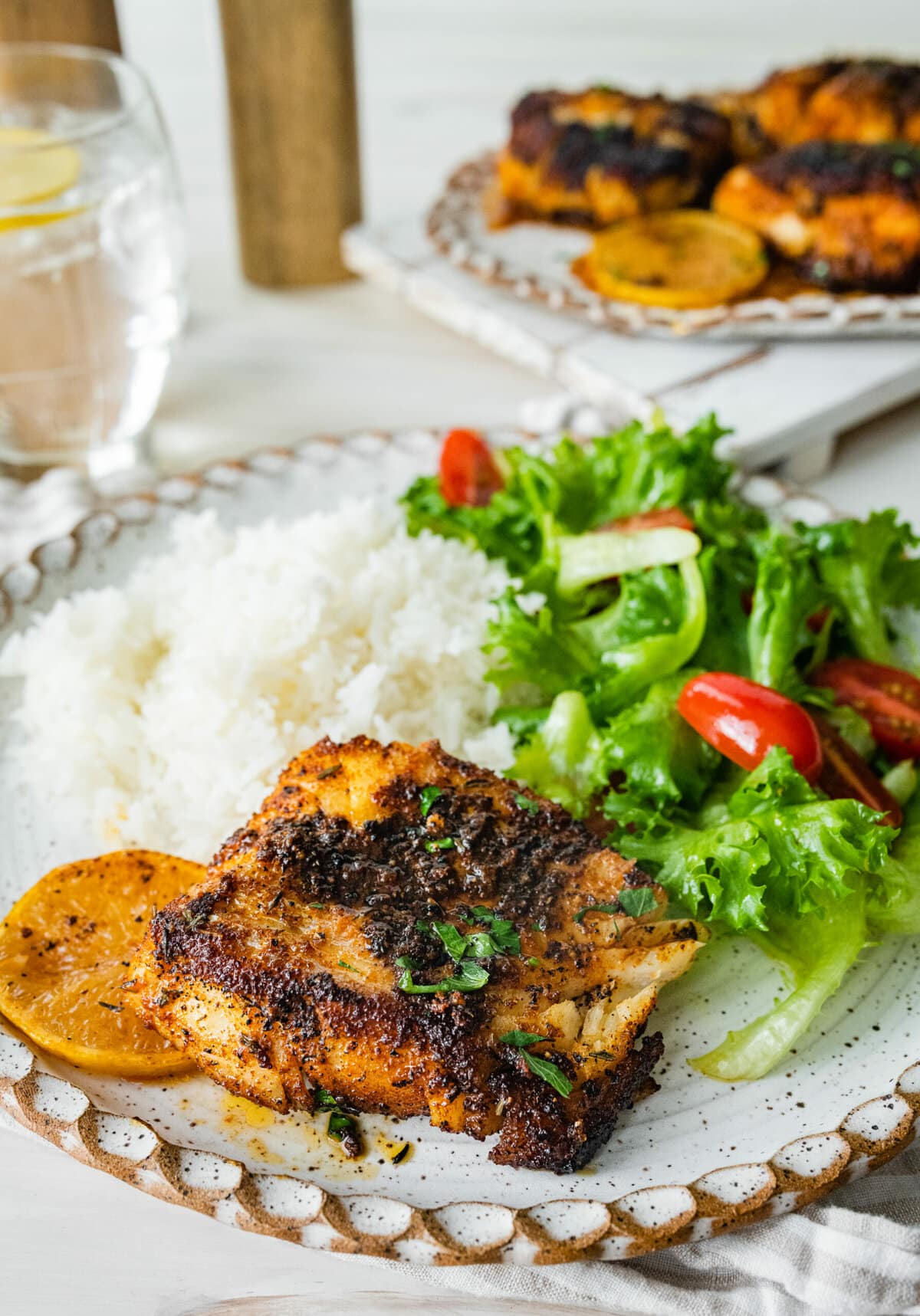platted blackened cod with white rice and green salad with tomatoes.