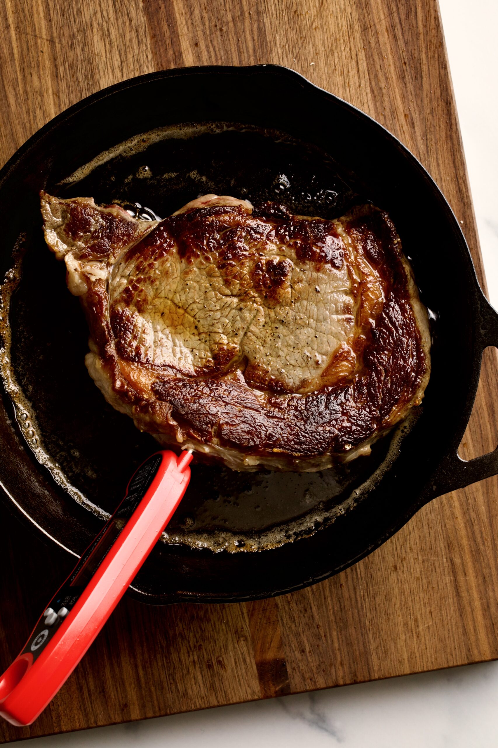 How to Cook Steak in a Pan (Perfect Recipe)- steak cooking a pan using a meat thermometer to check for doneness.