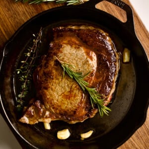 Pan-seared steak in a pan with garlic and herbs.